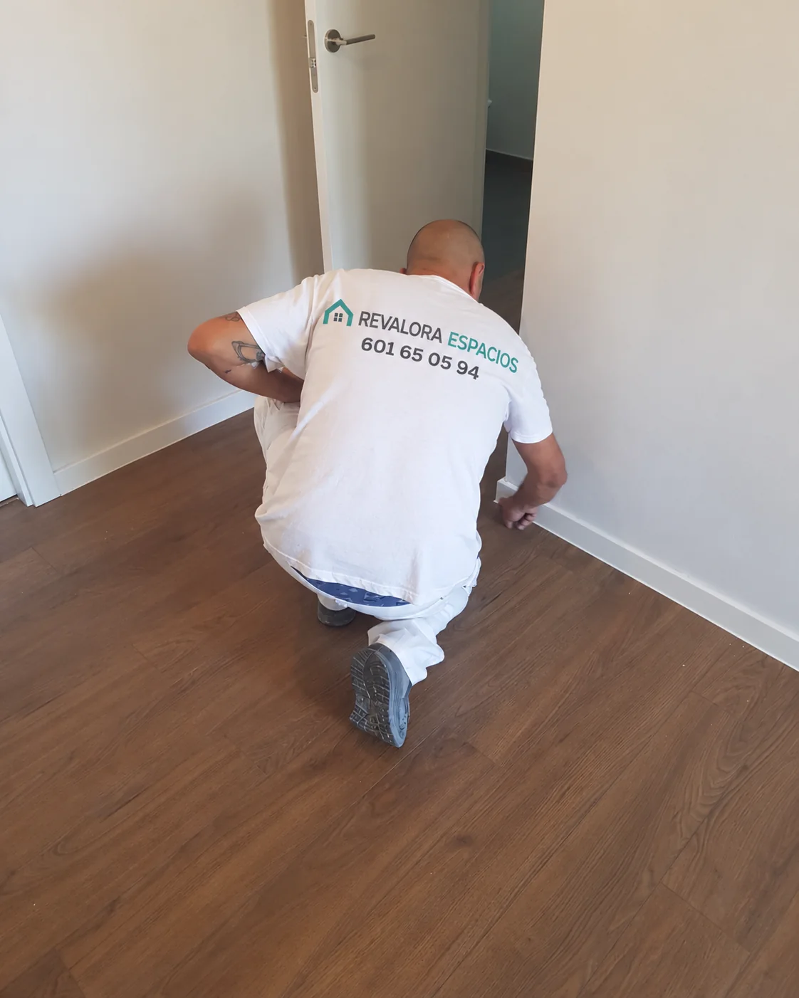 Profesional de REVALORA arrodillado trabajando en el remate de rodapiés junto a una pared interior de una vivienda.